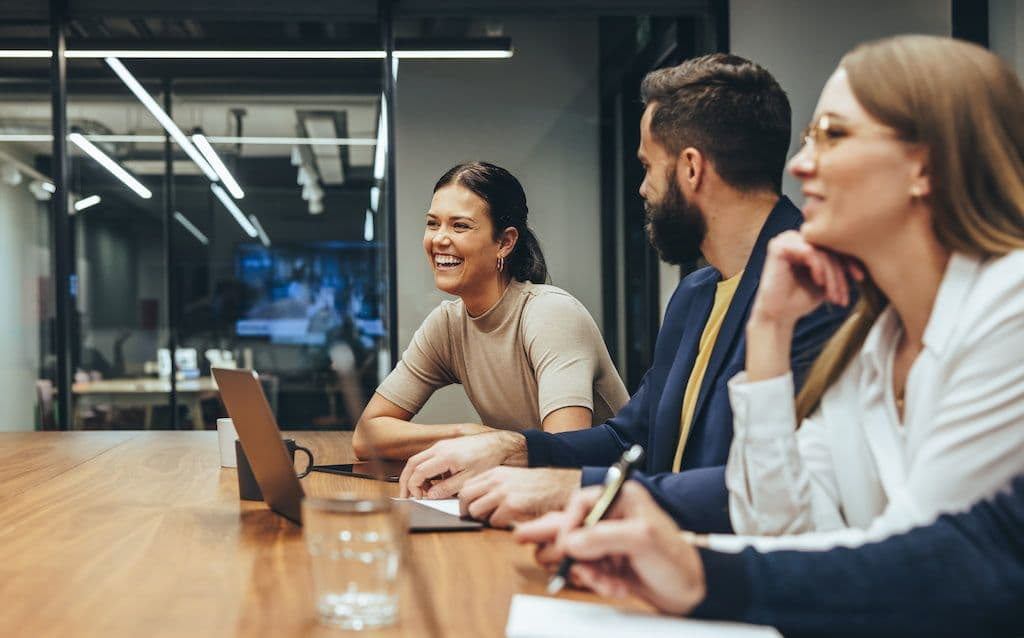 People smiling and talking during a meeting in a modern office.